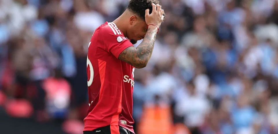 Jugador de fútbol con camiseta roja, preocupado en el campo