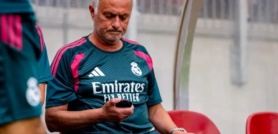 Entrenador de Real Madrid revisando su teléfono en el banquillo