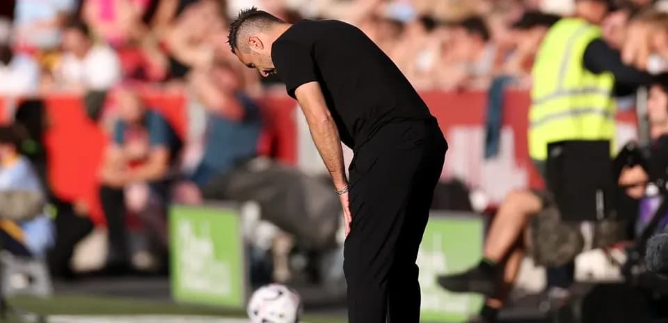 Entrenador agachado junto a balón en la línea de banda