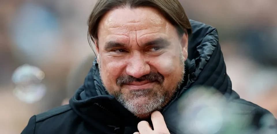 Entrenador con chaqueta oscura sonriendo en el banquillo