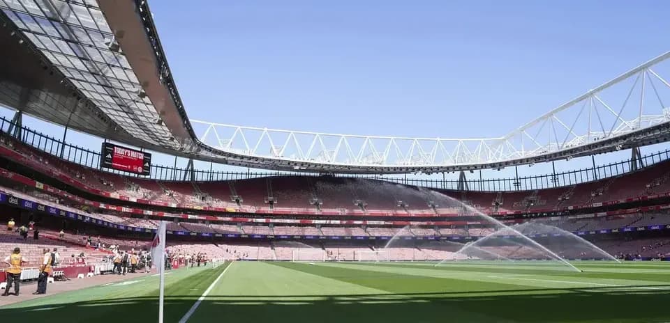 Estadio con césped regado y gradas vacías