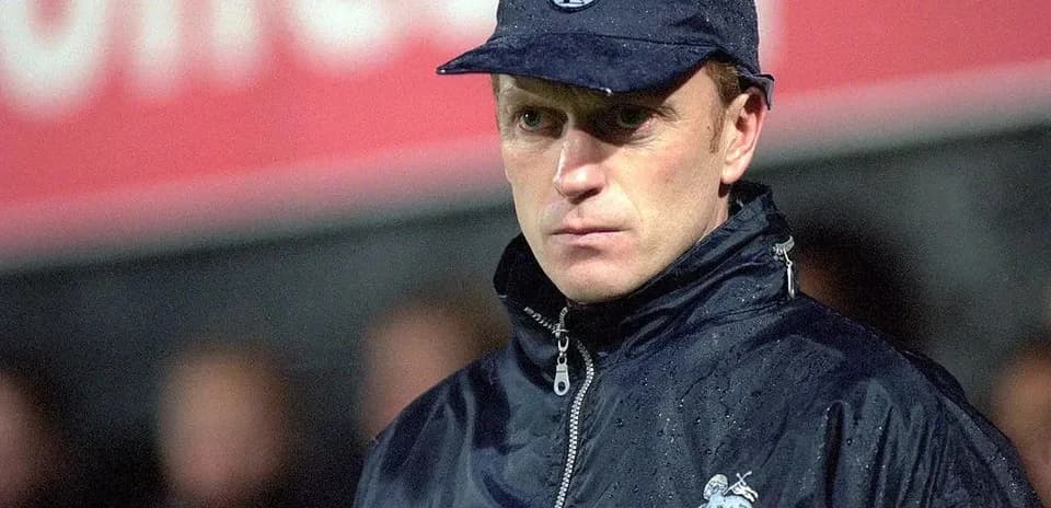 Entrenador de fútbol con abrigo y gorra en lluvia