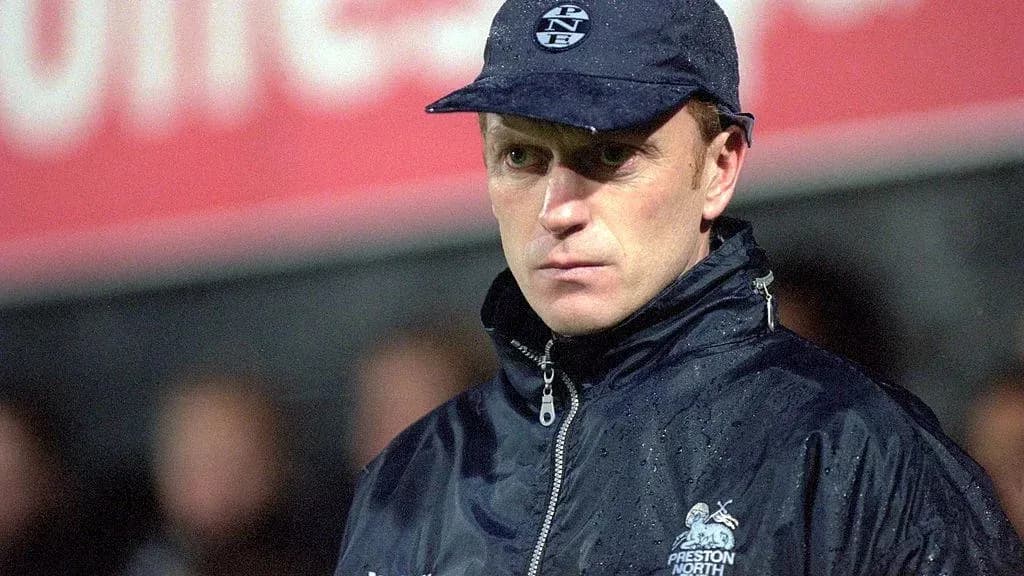 Entrenador de fútbol con abrigo y gorra en lluvia