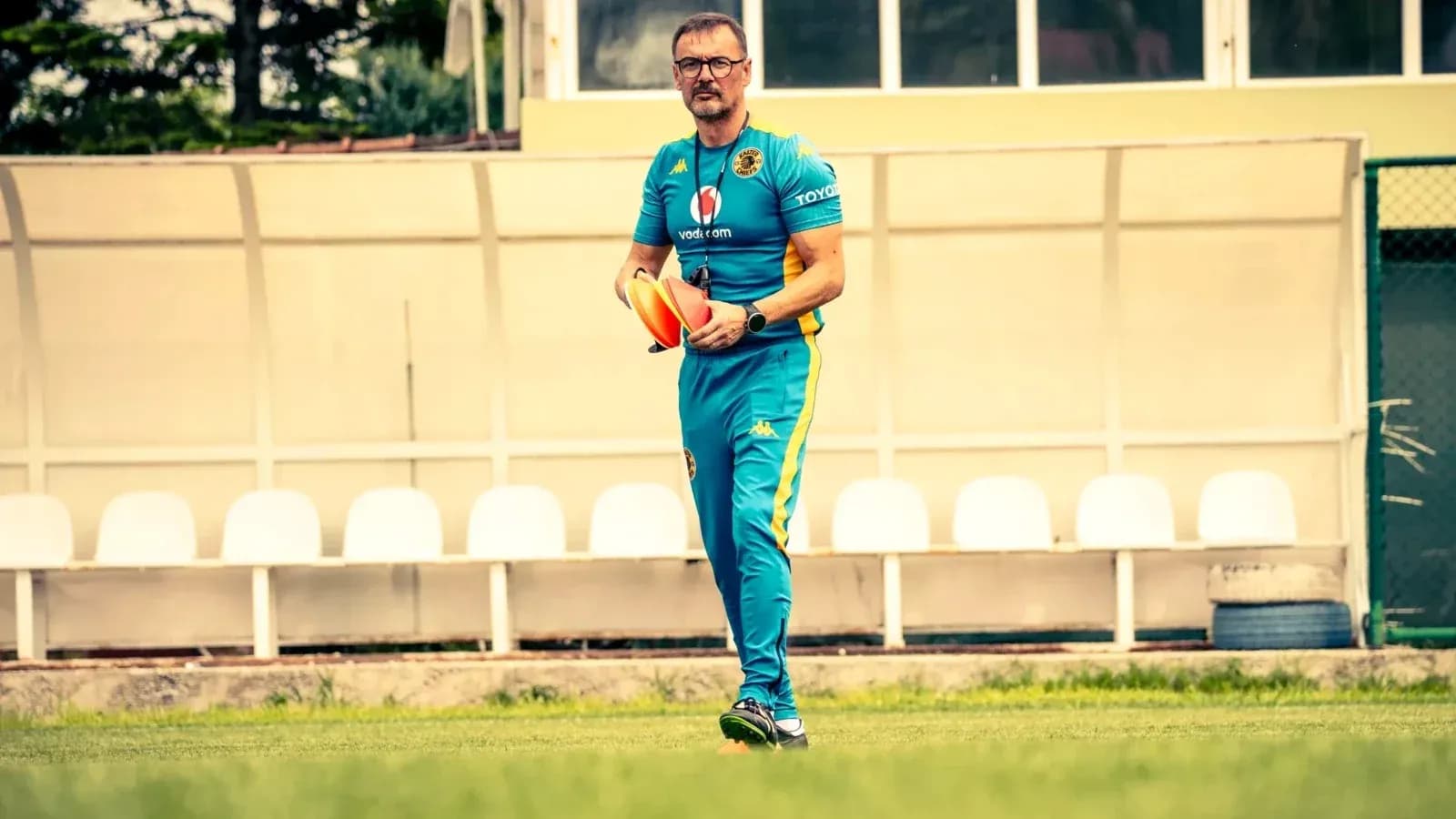 Entrenador caminando con conos de entrenamiento en campo