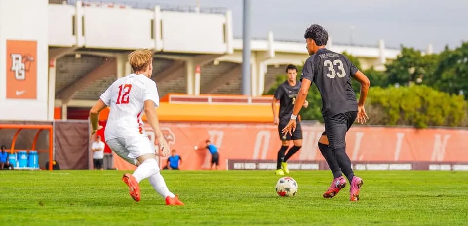 Jugador con balón y rival persiguiéndolo en el campo