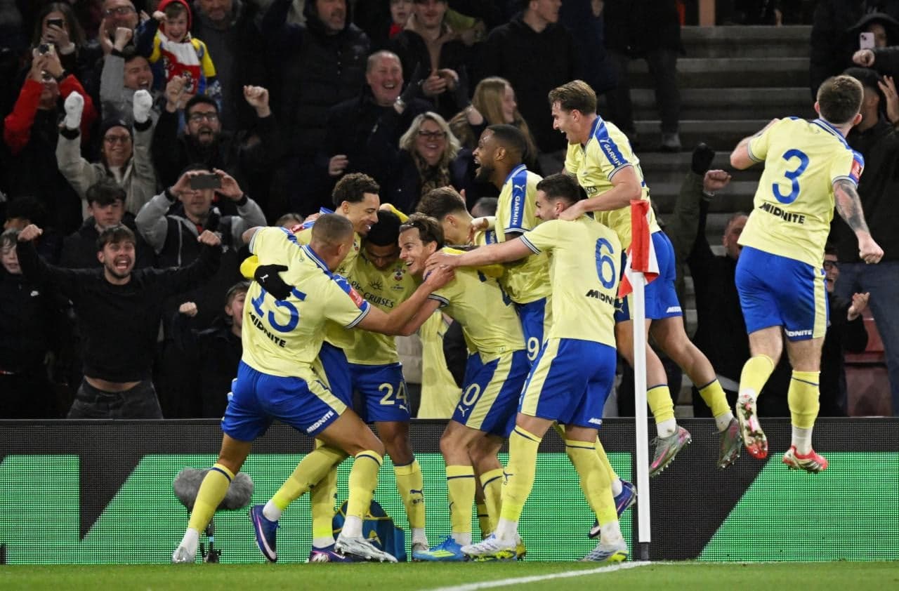 Jugadores celebrando un gol con aficionados de fondo