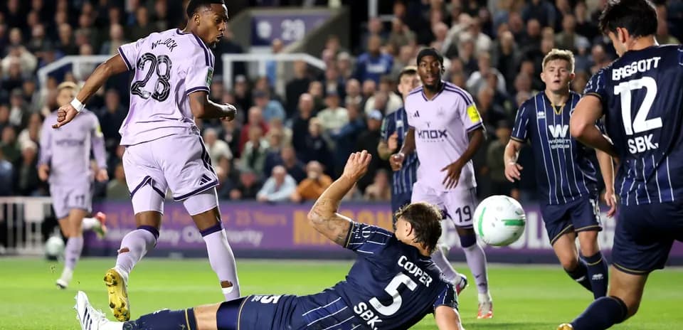 Jugador en uniforme morado dispara mientras defensor cae