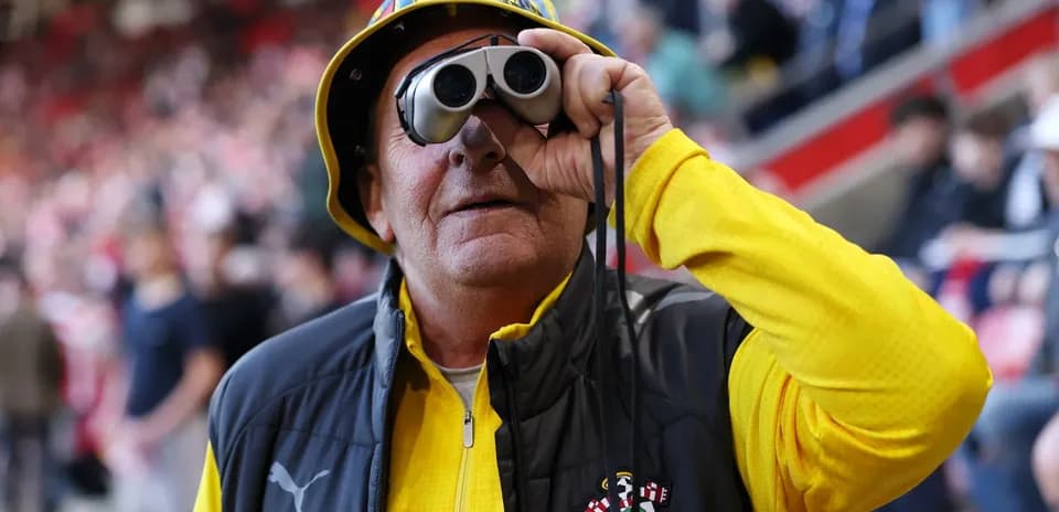 A fan wearing binoculars and a hat at stadium