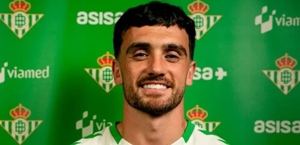 Jugador sonriendo frente a fondo del Real Betis