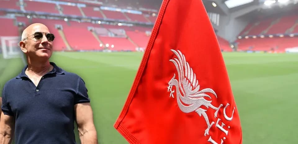 Hombre junto a bandera de Liverpool en estadio vacío
