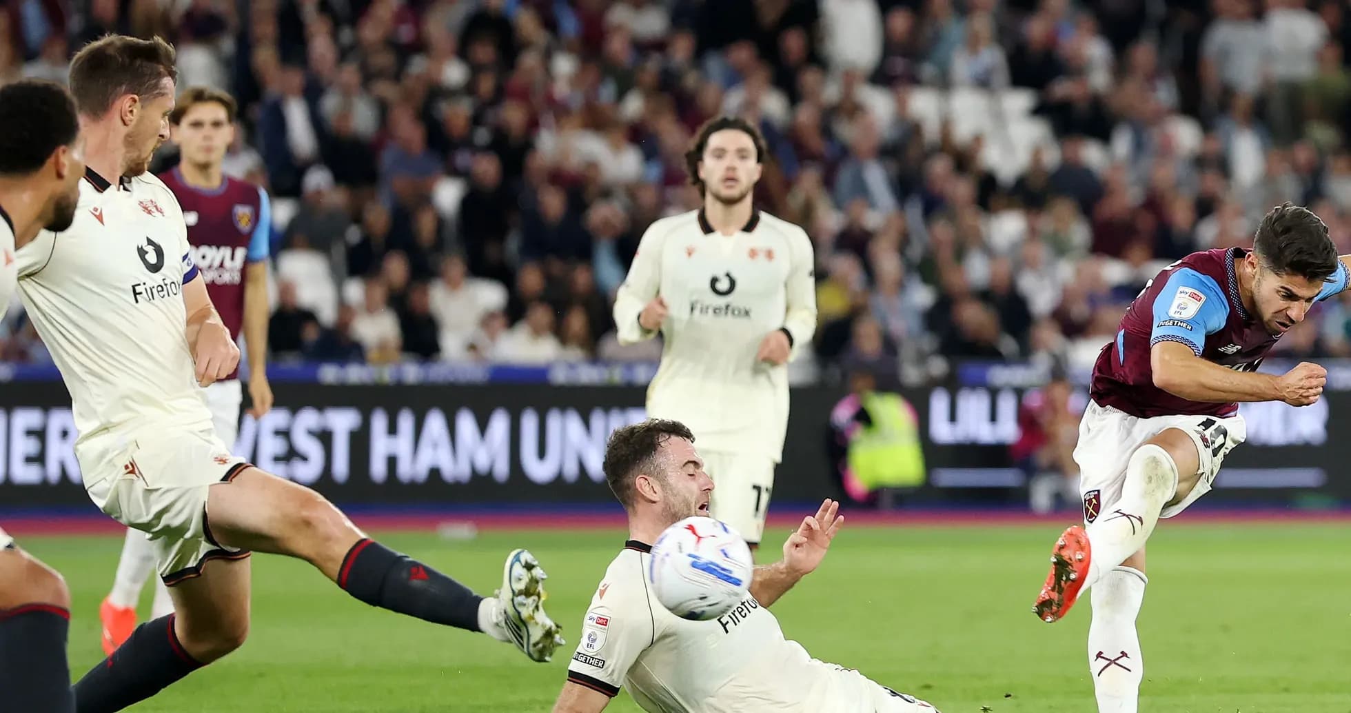 Jugador de West Ham chutando mientras rival cae al suelo