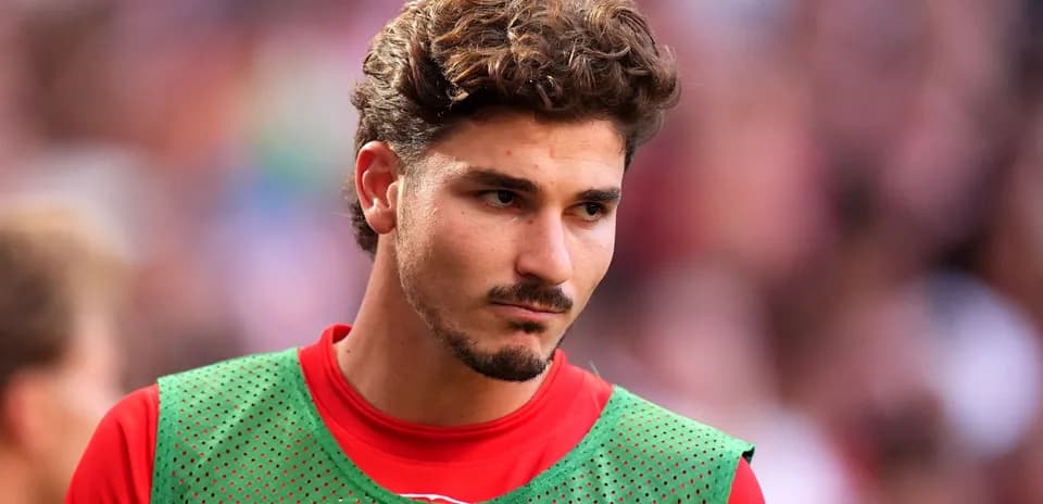 Jugador en la banca con camiseta roja y chaleco verde
