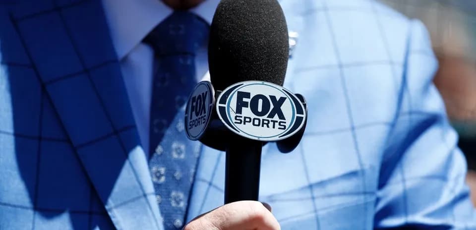 Mic with FOX Sports logo held in a blue suit
