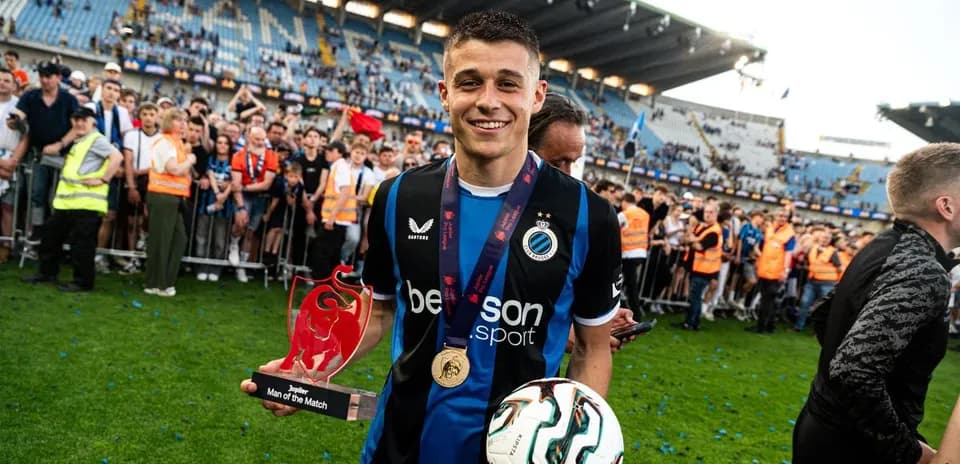 Jugador sosteniendo trofeo y balón en el campo