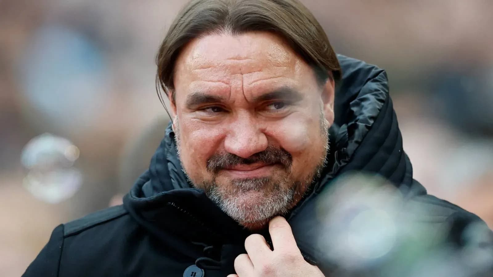 Entrenador con chaqueta oscura sonriendo en el banquillo Entrenador con chaqueta oscura sonriendo en el banquillo