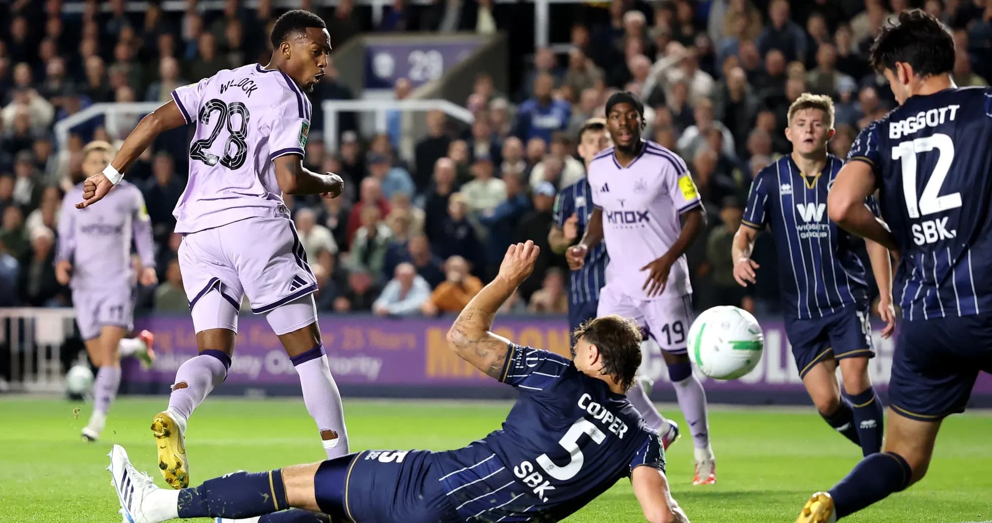 Jugador en uniforme morado dispara mientras defensor cae Jugador en uniforme morado dispara mientras defensor cae